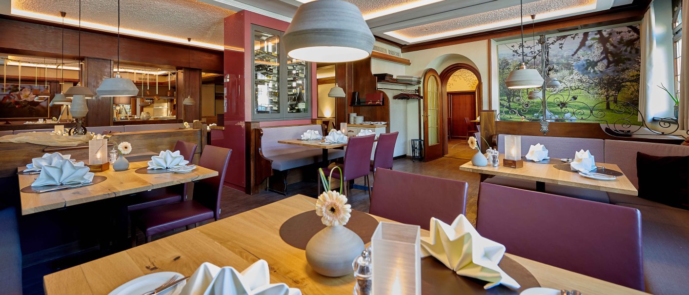 Elegantes Restaurant mit Holztischen, gefalteten Servietten und moderner Beleuchtung. Gemütliche Atmosphäre mit dekorativen Elementen und Wandbild., © Hotel Gasthof Hasen