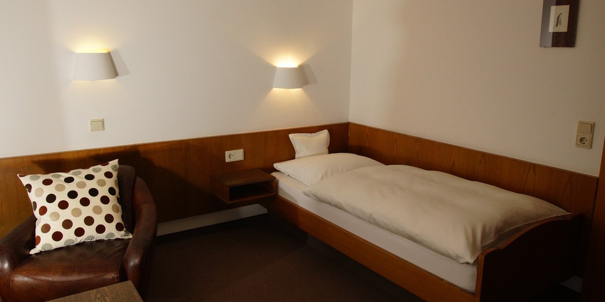 Ein gemütliches Einzelzimmer mit einem Bett, einem braunen Ledersessel mit gepunktetem Kissen und zwei Wandlampen., © Hotelmärchen Ein gemütliches Einzelzimmer mit einem Bett, einem braunen Ledersessel mit gepunktetem Kissen und zwei Wandlampen., © Hotelmärchen