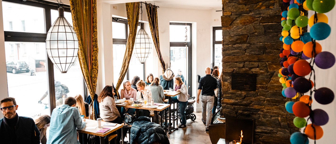 Gem&uuml;tliches Caf&eacute; mit gro&szlig;en Fenstern, Menschen an Tischen, bunte Kugeln an der Wand und ein Kamin. Warme, einladende Atmosph&auml;re., &copy; Stuttgart-Marketing GmbH, Sarah Schmid