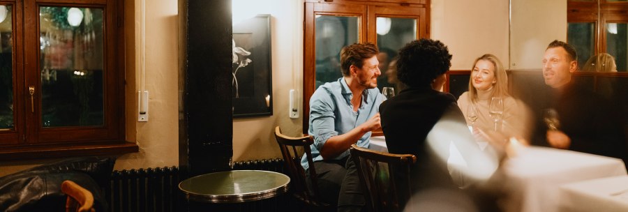 Four people are sitting in a cozy wine bar, chatting and enjoying wine. The atmosphere is warm and inviting., © © Stuttgart-Marketing GmbH, Alwin Maigler