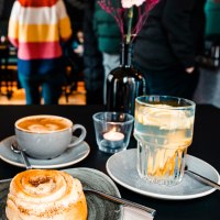 Ein Tisch in einem Café mit Zimtschnecke, Cappuccino und Zitronenwasser. Im Hintergrund sind unscharfe Personen zu sehen., © Stuttgart-Marketing GmbH, Sarah Schmid Ein Tisch in einem Café mit Zimtschnecke, Cappuccino und Zitronenwasser. Im Hintergrund sind unscharfe Personen zu sehen., © Stuttgart-Marketing GmbH, Sarah Schmid