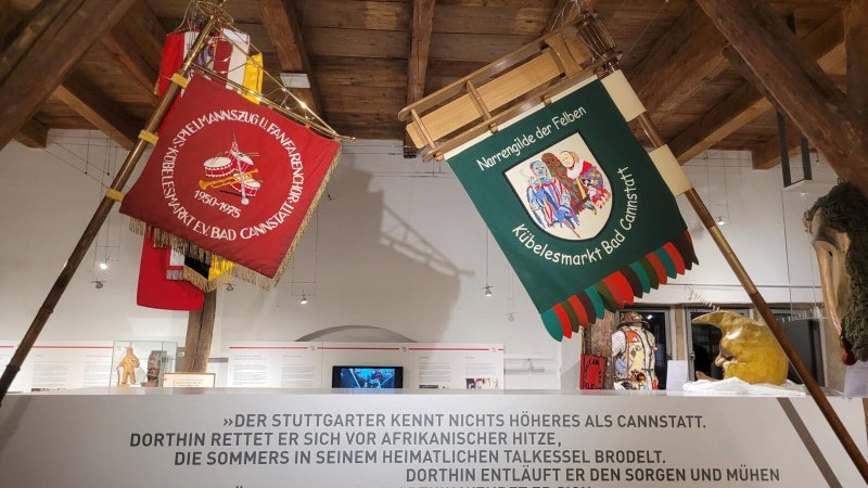 Traditionelle Fahnen und Masken im Stadtmuseum Bad Cannstatt. Ein Zitat von Heinrich Ebner ist an der Wand zu sehen., © StadtPalais