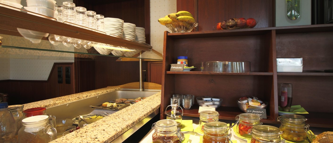 Breakfast buffet with various jams in jars, crockery on shelves and fruit bowl with bananas. Wooden furniture and bright lighting., © TOMAS Breakfast buffet with various jams in jars, crockery on shelves and fruit bowl with bananas. Wooden furniture and bright lighting., © TOMAS