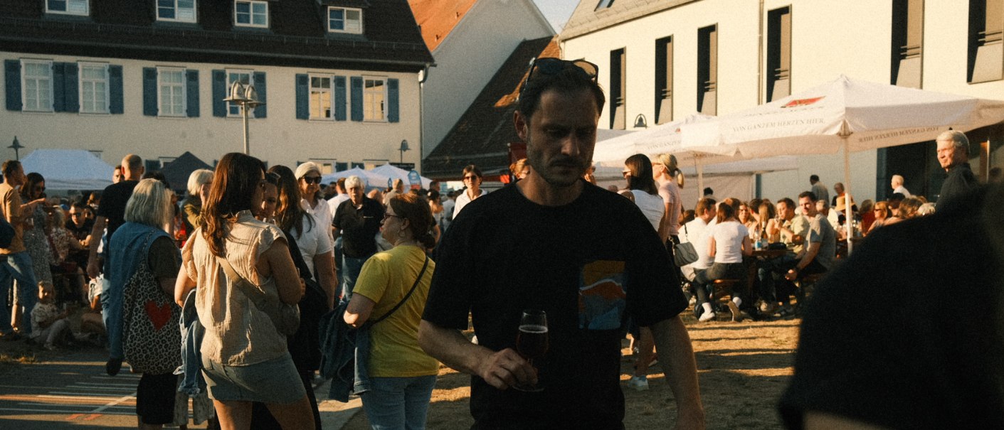 A lively scene at an outdoor wine festival, with lots of people chatting and sitting at tables. Parasols provide shade., &copy; MyDegerloch