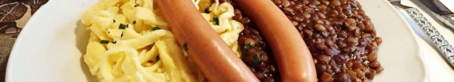 Ein Teller mit Linsen, Spätzle und zwei Würstchen, serviert auf einem Tisch mit Besteck., © TMBW, Susi Maier