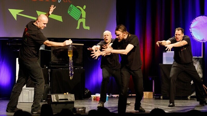 Vier Männer auf einer Bühne führen eine dynamische Physikshow vor. Einer hält eine Flasche, während die anderen gestikulieren. Im Hintergrund bunte Lichter., © Theaterhaus Stuttgart e.V. Vier Männer auf einer Bühne führen eine dynamische Physikshow vor. Einer hält eine Flasche, während die anderen gestikulieren. Im Hintergrund bunte Lichter., © Theaterhaus Stuttgart e.V.