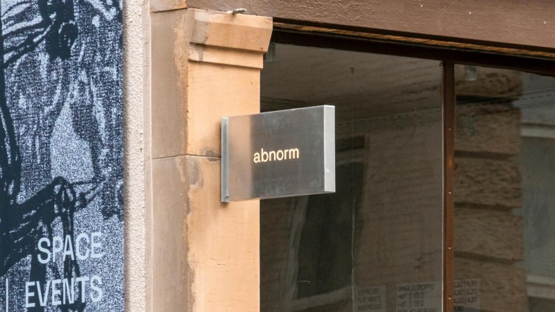 Ein Metallschild mit der Aufschrift 'abnorm' h&auml;ngt an einer Wand. Daneben ist ein Kunstplakat zu sehen., &copy; SMG, Sarah Schmid
