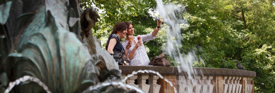 Two women take a selfie at the Galatea Fountain, holding ice cream. Trees and a splash of water can be seen in the background., &copy; Stuttgart-Marketing GmbH Christoph D&uuml;pper