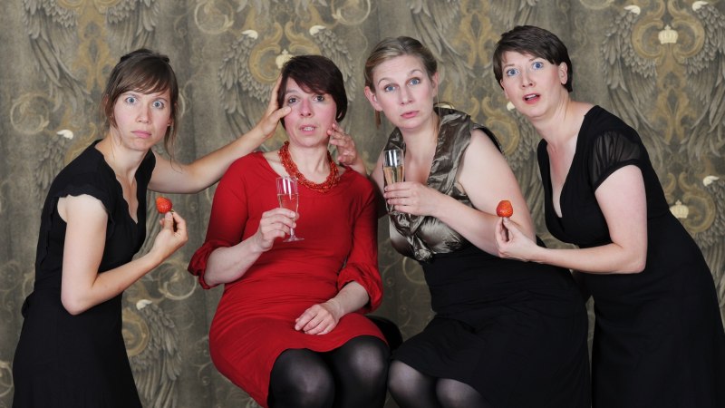 Four women in elegant clothes pose with surprised expressions on their faces, holding strawberries and champagne glasses in front of a decorative background., &copy; Yakup Zeyrek