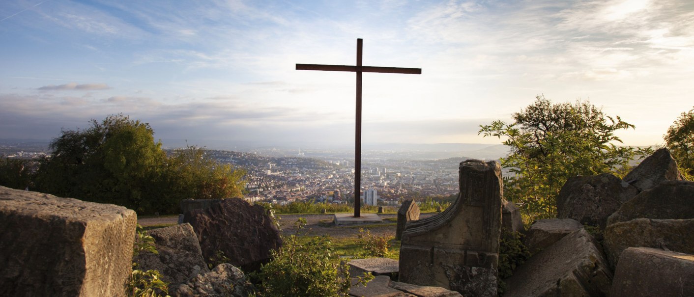 Ein Kreuz auf dem Birkenkopf in Stuttgart, umgeben von Tr&uuml;mmern, mit Blick auf die Stadt im Hintergrund bei Sonnenuntergang., &copy; Stuttgart-Marketing GmbH, Jean-Claude Winkler