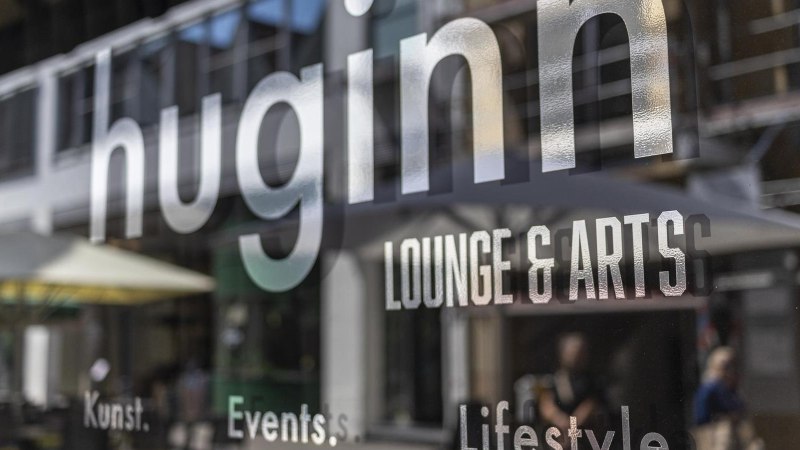 Spiegelung des Schriftzugs 'huginn LOUNGE & ARTS' auf einer Glasoberfl&auml;che, im Hintergrund unscharfe Stra&szlig;enszene., &copy; SMG, Sarah Schmid