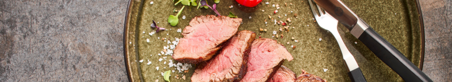 A plate with sliced steak, two cherry tomatoes and cutlery on a rustic base., © MAREDO