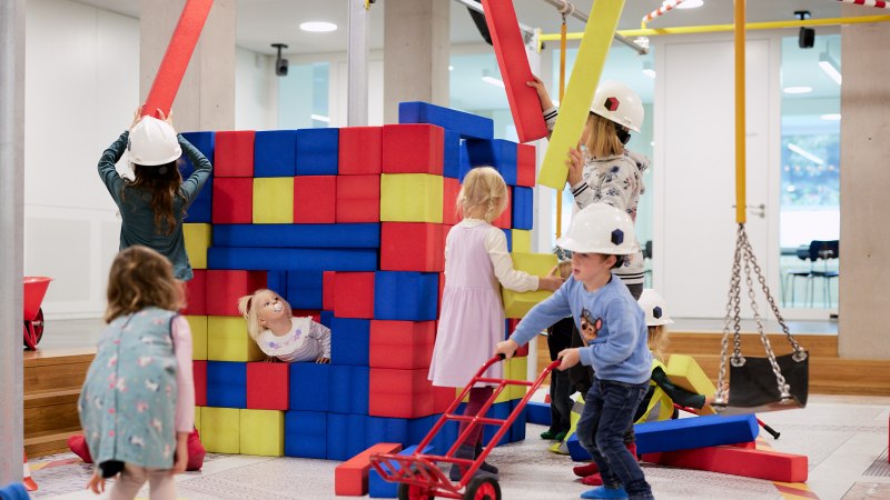 Kinder spielen auf einer Indoor-Baustelle mit bunten Schaumstoffblöcken. Sie tragen Bauhelme und haben Spaß beim Bauen und Spielen., © Julia Ochs
