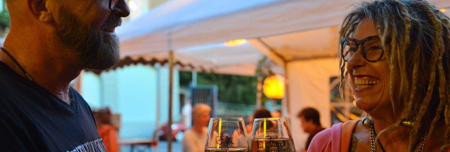 Zwei Personen stoßen mit Weingläsern an und lächeln sich an, während sie unter einem Zelt sitzen., © Weingut Ruoff Zwei Personen stoßen mit Weingläsern an und lächeln sich an, während sie unter einem Zelt sitzen., © Weingut Ruoff