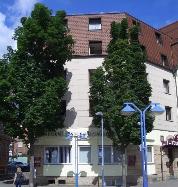 Das Hotel Feuerbacher Hof mit Bäumen davor und blauen Straßenlaternen. Eine Person überquert den Zebrastreifen., © Feuerbacher Hof