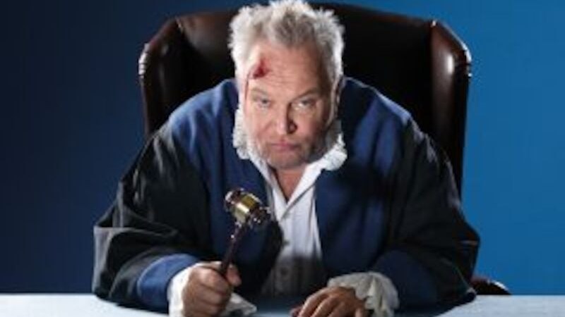 Ein Mann in einer Richterrobe sitzt an einem Tisch und hält einen Hammer. Er hat eine Verletzung an der Stirn und wirkt nachdenklich., © Altes Schauspielhaus und Komödie im Marquardt e.V. Ein Mann in einer Richterrobe sitzt an einem Tisch und hält einen Hammer. Er hat eine Verletzung an der Stirn und wirkt nachdenklich., © Altes Schauspielhaus und Komödie im Marquardt e.V.