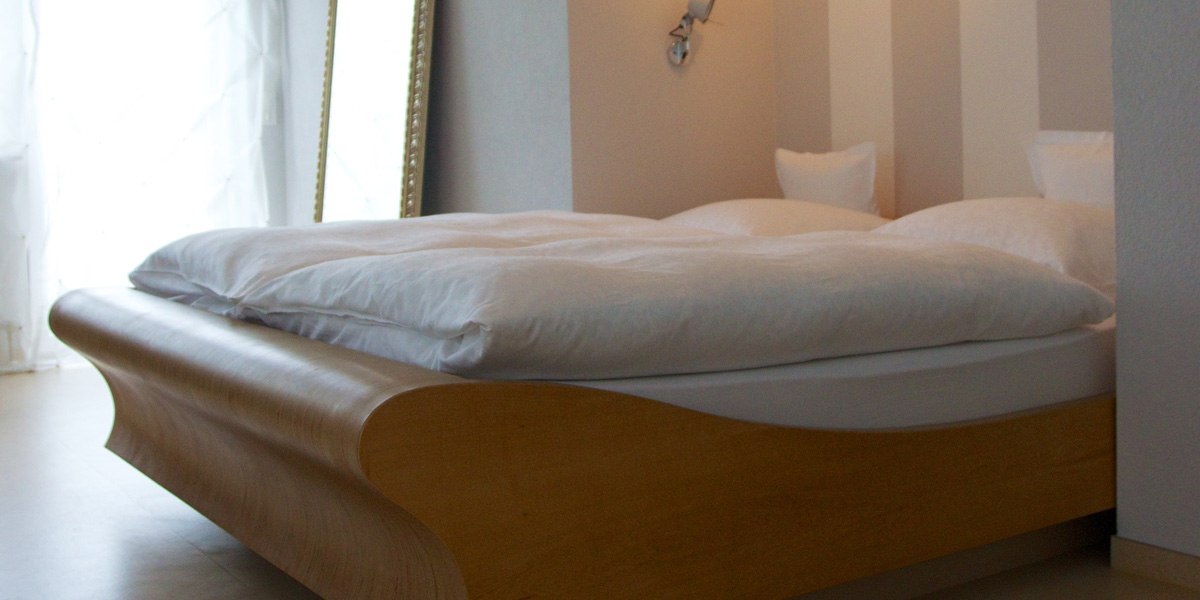 Ein modernes Doppelbett mit weißer Bettwäsche in einem hellen Zimmer mit gestreifter Tapete und einem großen Spiegel., © Hotelmärchen Ein modernes Doppelbett mit weißer Bettwäsche in einem hellen Zimmer mit gestreifter Tapete und einem großen Spiegel., © Hotelmärchen