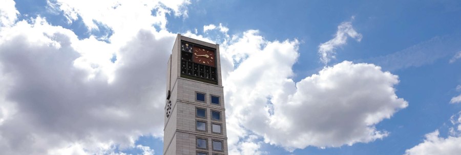 A modern building with a tall clock tower and lots of windows. The sky is blue with a few clouds., &copy; Fei Shiyu