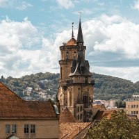 Die Stiftskirche mit ihrem markanten Turm erhebt sich über die Dächer der Stadt, umgeben von grünen Hügeln und einem bewölkten Himmel., © Stuttgart-Marketing GmbH, Sarah Schmid Die Stiftskirche mit ihrem markanten Turm erhebt sich über die Dächer der Stadt, umgeben von grünen Hügeln und einem bewölkten Himmel., © Stuttgart-Marketing GmbH, Sarah Schmid