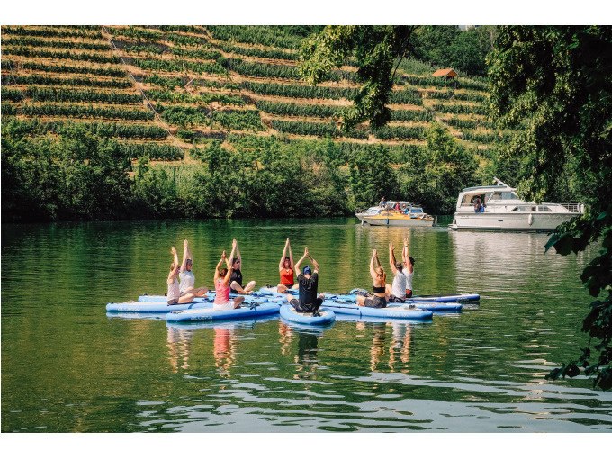 Menschen praktizieren Yoga auf SUP-Boards auf einem Fluss, umgeben von Weinbergen und einem vorbeifahrenden Boot., &copy; Cool-Tours StattReisen