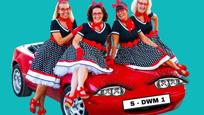 Vier Frauen in gepunkteten Retro-Kleidern sitzen auf einem roten Auto mit aufgemalten Wimpern und einem Nummernschild 'S - DWM 1'., © Theaterhaus Stuttgart e.V.