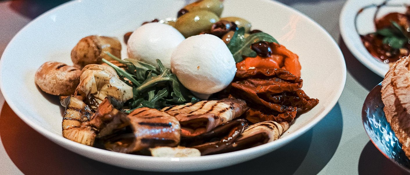 Ein Teller mit Antipasti: Mozzarella, gegrilltes Gemüse, Rucola und Oliven. Farbenfrohe und appetitliche Präsentation., © Italo Disco, Stuttgart