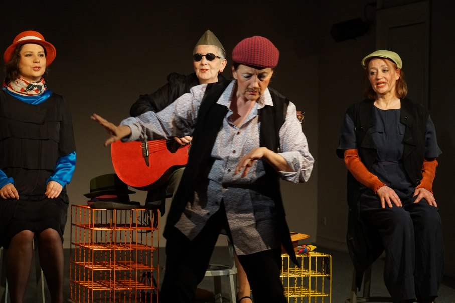 Eine Gruppe von vier Personen auf einer B&uuml;hne. Eine Person spielt Gitarre, eine tanzt, zwei sitzen. Alle tragen bunte H&uuml;te und Kost&uuml;me., &copy; Katja Ritter