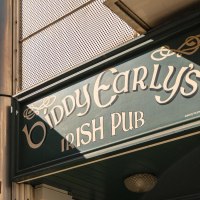 Eingang von Biddy Early's Irish Pub mit grünem Schild und Guinness-Werbung. Sonneneinstrahlung auf der Fassade., © SMG, Sarah Schmid