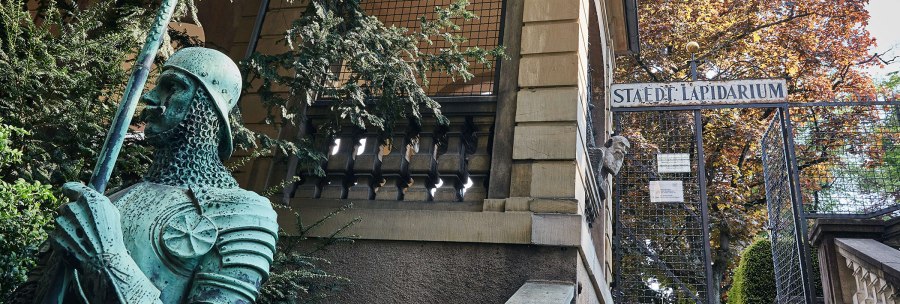 Eingang zum Städtischen Lapidarium mit einer grünen Ritterstatue im Vordergrund und einem Tor im Hintergrund., © Städtisches Lapidarium, Foto Julia Ochs