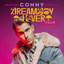 Ein Mann in einer Jacke mit Fellkragen vor einem pinken Hintergrund. Text: CONNY - DREAM BOY 4EVER TOUR., © links im Bild