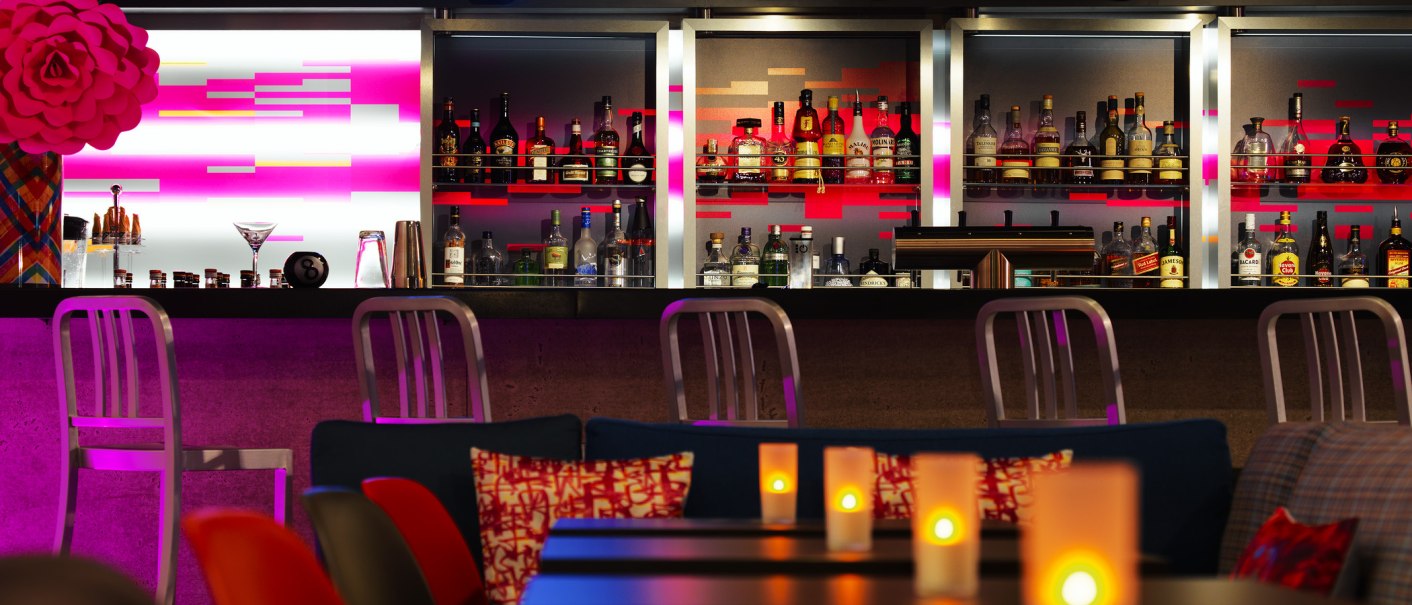 Moderne Bar mit Neon-Schriftzug 'W XYZ', beleuchtetem Tresen und gemütlicher Atmosphäre. Kerzen auf den Tischen sorgen für stimmungsvolles Licht., © Aloft Stuttgart