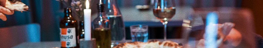 A table in a restaurant with several pizzas, drinks and a burning candle. Glasses and a bottle can be seen in the background., &copy; Italo Disco, Stuttgart