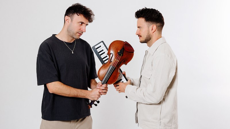 Zwei Männer stehen sich gegenüber und halten gemeinsam eine Geige und eine Melodica. Sie schauen sich ernst an., © Renitenztheater Stuttgart e.V. Zwei Männer stehen sich gegenüber und halten gemeinsam eine Geige und eine Melodica. Sie schauen sich ernst an., © Renitenztheater Stuttgart e.V.