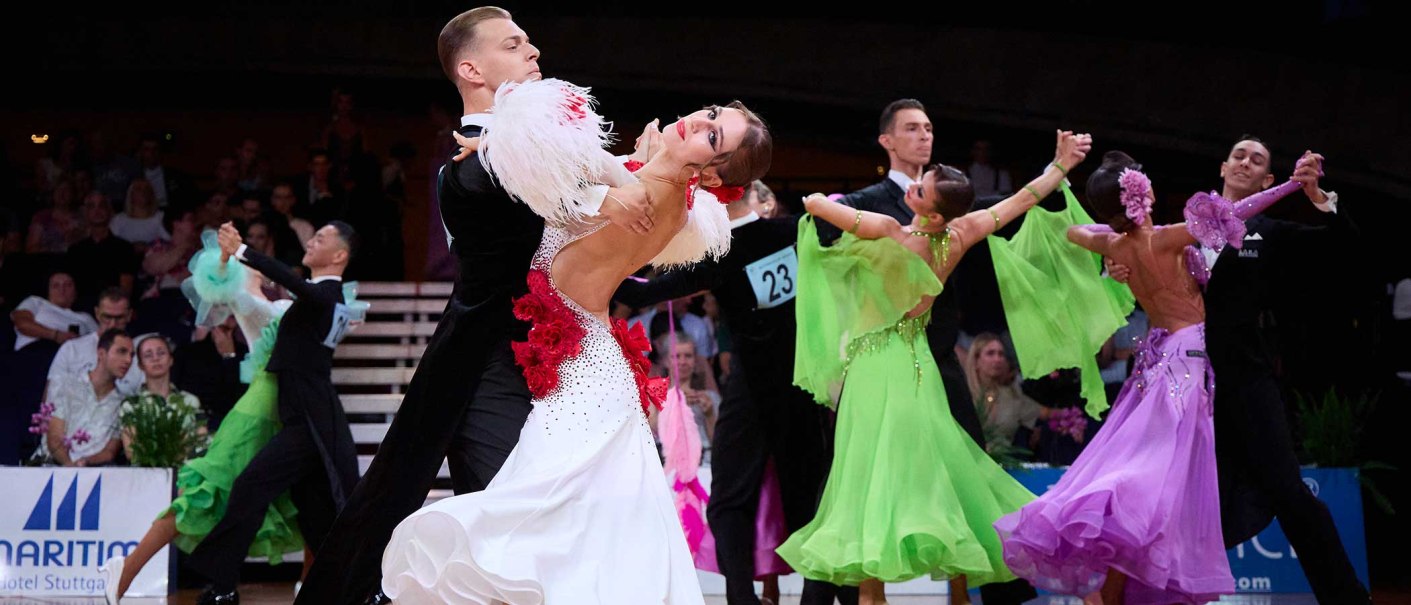 Tanzpaare in eleganten Kost&uuml;men tanzen bei der German Open Championship. Frauen tragen bunte Kleider, M&auml;nner schwarze Anz&uuml;ge. Zuschauer im Hintergrund., &copy; GOC, Fotograf: Bob van Ooik