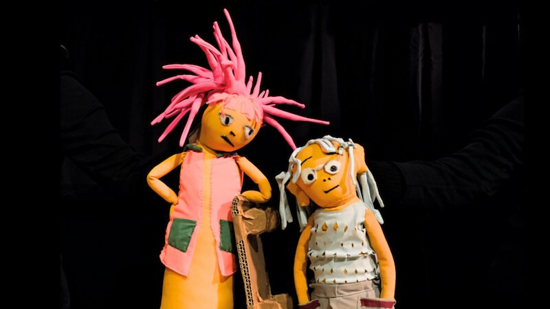 Zwei bunte Puppen mit auffälligen Frisuren stehen vor einem schwarzen Hintergrund. Eine Puppe hat pinke Haare, die andere weiße., © FITZ Das Theater animierter Formen Zwei bunte Puppen mit auffälligen Frisuren stehen vor einem schwarzen Hintergrund. Eine Puppe hat pinke Haare, die andere weiße., © FITZ Das Theater animierter Formen