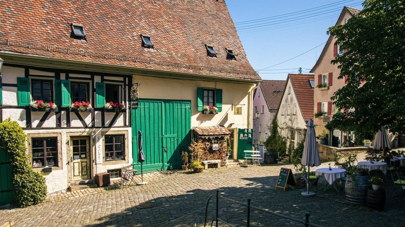 An idyllic courtyard in Nürtingen's old town with a half-timbered house, green shutters and cozy seating under a tree., © Stuttgart-Marketing GmbH, Sarah Schmid An idyllic courtyard in Nürtingen's old town with a half-timbered house, green shutters and cozy seating under a tree., © Stuttgart-Marketing GmbH, Sarah Schmid