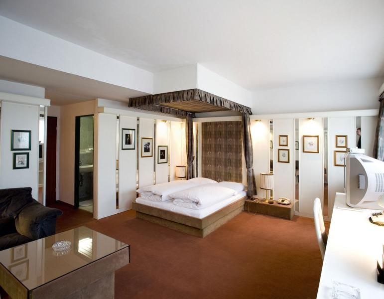 A spacious hotel room with a four-poster bed, a desk, a sofa, and decorative paintings on the walls., &copy; Hotel Spahr