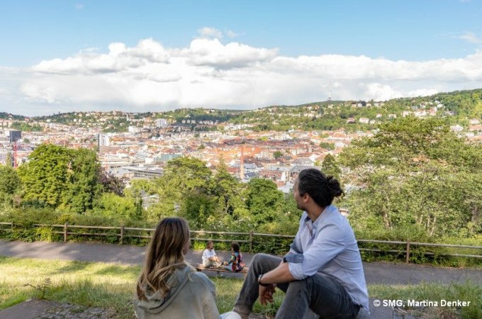 Zwei Personen sitzen auf einer Bank und genießen den Ausblick auf Stuttgart. Im Hintergrund sind grüne Hügel und die Stadtlandschaft zu sehen., © Stuttgart Marketing GmbH Zwei Personen sitzen auf einer Bank und genießen den Ausblick auf Stuttgart. Im Hintergrund sind grüne Hügel und die Stadtlandschaft zu sehen., © Stuttgart Marketing GmbH