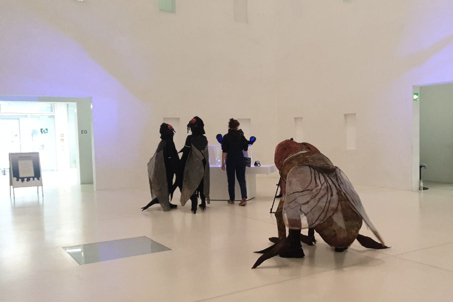 Zwei Personen in Fliegenkost&uuml;men und eine weitere Person in einem modernen, wei&szlig;en Ausstellungsraum. Die Szene wirkt surreal und k&uuml;nstlerisch., &copy; Foto: Stadtbibliothek Stuttgart