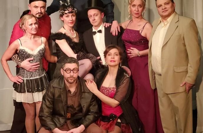 Neun Personen in verschiedenen Kostümen posieren auf einer Bühne. Sie tragen elegante und thematische Kleidung, passend zu einer Theateraufführung., © Theater Atelier Neun Personen in verschiedenen Kostümen posieren auf einer Bühne. Sie tragen elegante und thematische Kleidung, passend zu einer Theateraufführung., © Theater Atelier