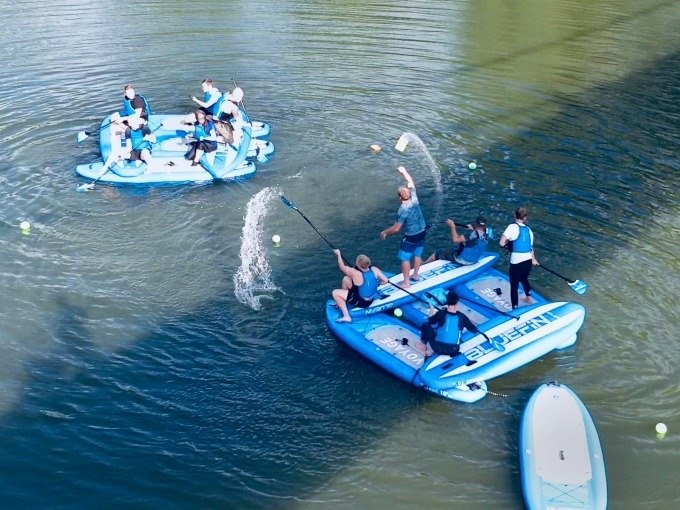 Two groups on blue SUP boards play in the water. Some people splash water with paddles while others watch., © Cool-Tours StattReisen Two groups on blue SUP boards play in the water. Some people splash water with paddles while others watch., © Cool-Tours StattReisen