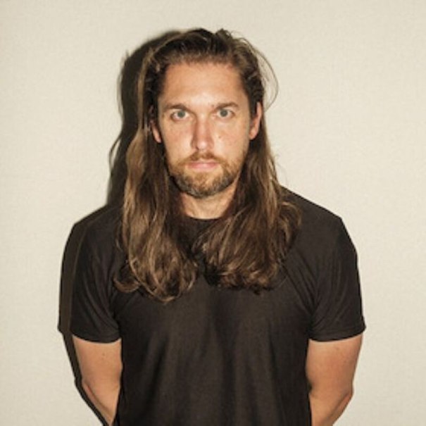 A man with long hair and a beard wears a black T-shirt and stands in front of a neutral background., &copy; Theaterhaus Stuttgart e.V.