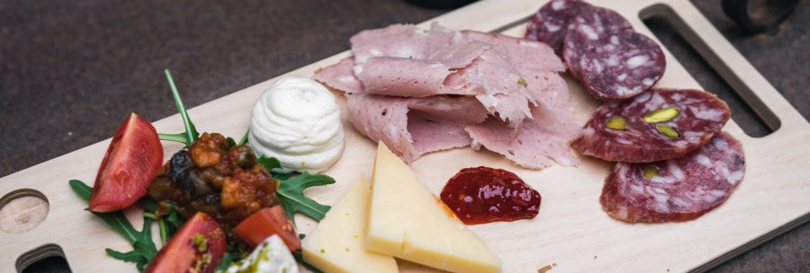 A wooden platter with ham, salami, cheese, tomatoes and rocket. Next to it is a bottle of beer labeled 'Bellabionda Helles'., © CELEBRE A wooden platter with ham, salami, cheese, tomatoes and rocket. Next to it is a bottle of beer labeled 'Bellabionda Helles'., © CELEBRE