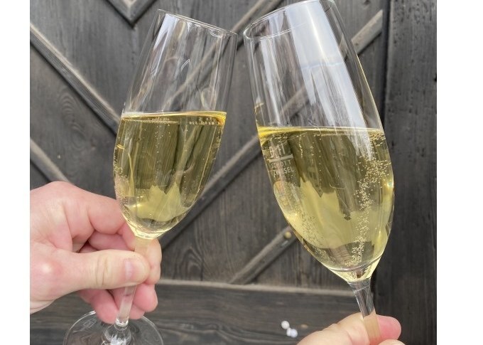 Zwei gef&uuml;llte Sektgl&auml;ser sto&szlig;en vor einem dunklen Holzhintergrund an. Die Gl&auml;ser sind mit prickelndem Sekt gef&uuml;llt., &copy; Weingenuss Stuttgart