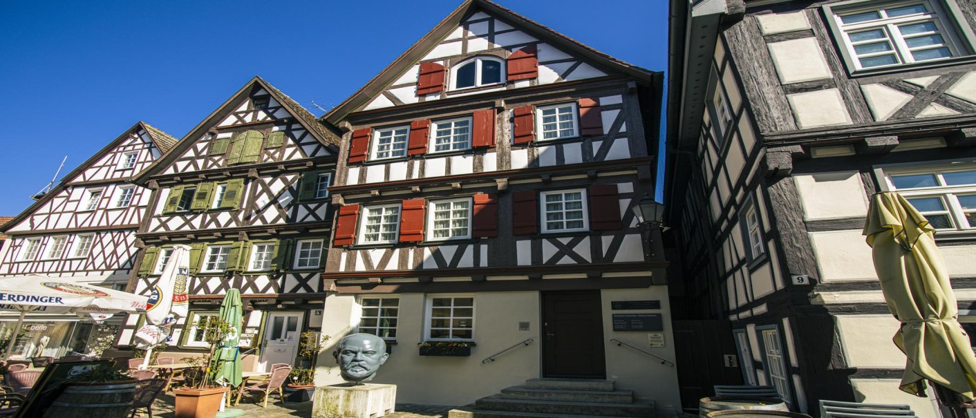 Fachwerkhäuser in Schorndorf bei sonnigem Wetter. Eine Büste steht vor einem der Häuser. Klare blaue Himmel im Hintergrund., © SMG Stuttgart Marketing GmbH - Sarah Schmid Fachwerkhäuser in Schorndorf bei sonnigem Wetter. Eine Büste steht vor einem der Häuser. Klare blaue Himmel im Hintergrund., © SMG Stuttgart Marketing GmbH - Sarah Schmid