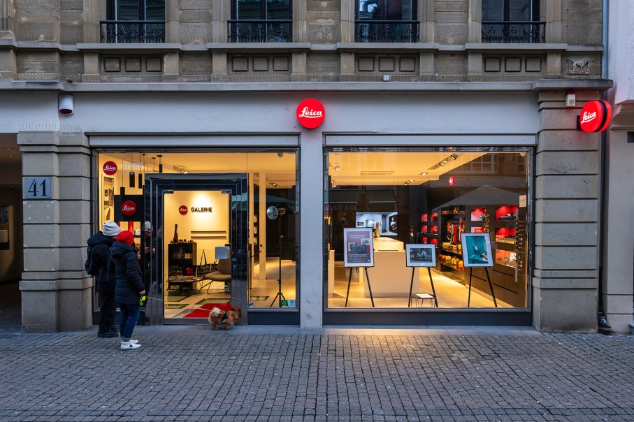 Leica Galerie und Store in der Calwer Straße 41 mit beleuchtetem Schaufenster. Zwei Personen und ein Hund stehen davor., © Holger Strehlow