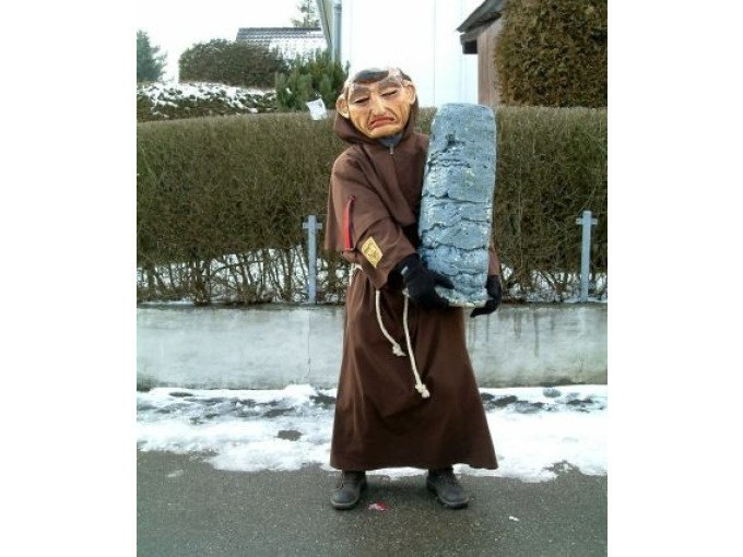 Person in braunem Kostüm mit Maske hält einen großen grauen Stein. Schnee liegt am Boden, Hecke im Hintergrund., © Cool-Tours StattReisen Person in braunem Kostüm mit Maske hält einen großen grauen Stein. Schnee liegt am Boden, Hecke im Hintergrund., © Cool-Tours StattReisen