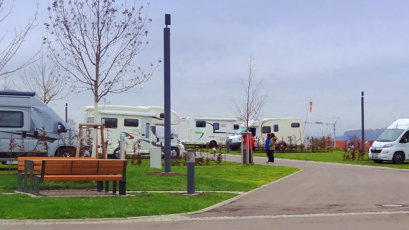 Wohnmobilstellplatz mit mehreren Wohnmobilen, kahlen Bäumen und einer Bank. Zwei Personen stehen auf dem Weg. Trübes Wetter., © Panorama Therme Beuren, Birgit Eschment