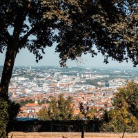 Panoramablick auf eine Stadt mit B&auml;umen im Vordergrund, die den Blick einrahmen. Eine Person sitzt auf einer Bank und genie&szlig;t die Aussicht., &copy; Stuttgart-Marketing GmbH, Sarah Schmid