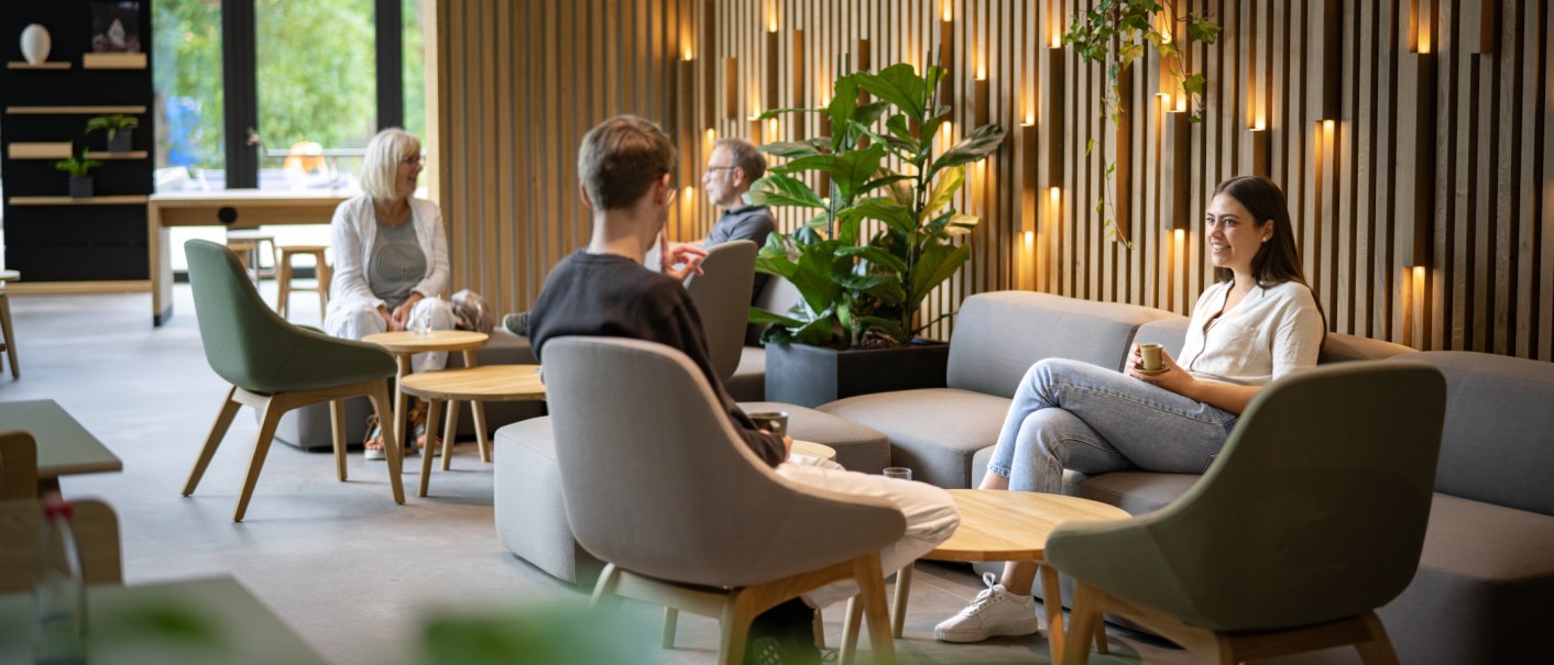 A modern café with wooden walls and plants. People are sitting comfortably on sofas, chatting over drinks., © STIHL Markenwelt A modern café with wooden walls and plants. People are sitting comfortably on sofas, chatting over drinks., © STIHL Markenwelt
